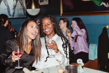 Two female friends laugh while drinking wine in a bar