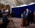 Donald Trump stands behind a lectern during a press conference. Members of the press reach out their hands to ask a question