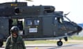A person almost completely covered in gear, from a helmet with goggles and mouthpiece to a dark green uniform, appears to walk away from a helicopter.