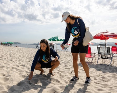 Two women collect sand samples on a beach.