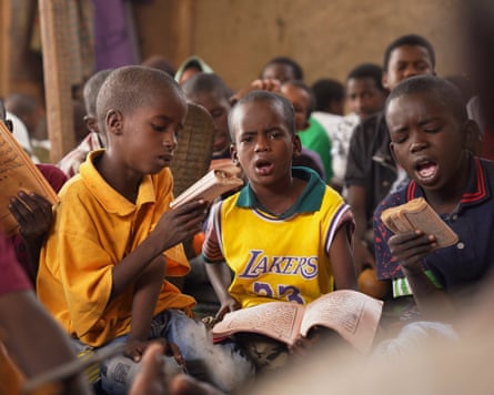 Young boys seated on the floor chanting, some reading from books with Arabic script
