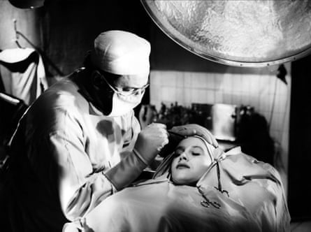 Doctor Genessier, a surgeon in gown and mask, leans over a patient under an operating light in Eyes Without a Face