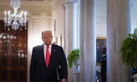 Man in suit and red tie stands with chandelier and columns in background