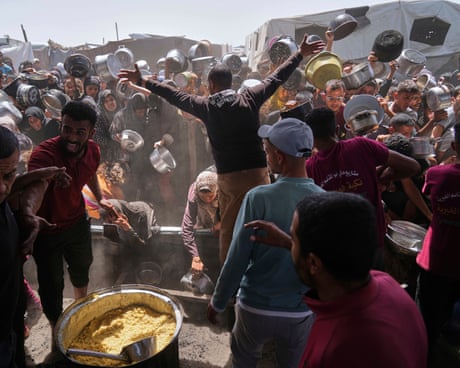 A group of Palestinians, many holding pots, clamour for food in front of a seller