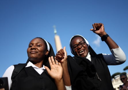Two nuns hold their hands up, one cheering, at the Vatican; they are both young black women and look happy.
