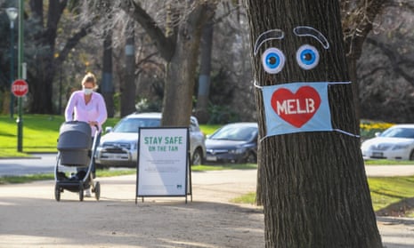 A woman pushes a pram past a large face mask pinned to a tree in Melbourne.