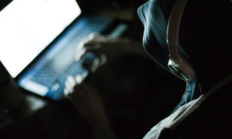 A hooded man typing into a laptop