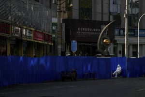 A worker in protective clothing keeps watch along metal barriers set up around the shuttered shophouses that were locked down as part of Covid-19 controls in Beijing
