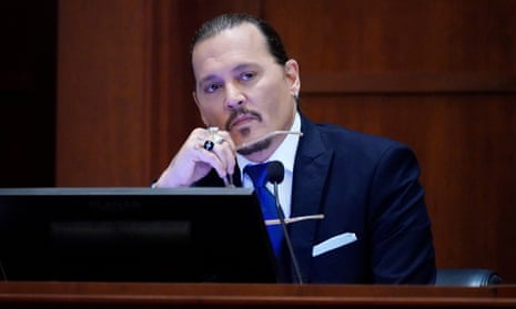 Actor Johnny Depp sits on the stand in a courtroom, leaning his chin on one hand which is holding a pair of glasses.