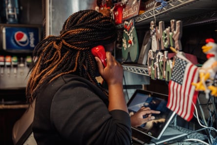woman inside a restaurant holds up a red phone to ear as she taps on a tablet