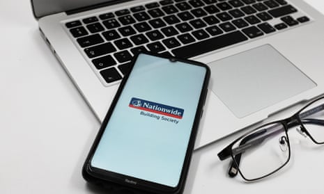 Nationwide Building Society bank logo is displayed on a smartphone screen above a notebook next to glasses and a Macbook