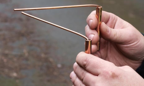 A water engineer uses copper divining rods to trace the course of an underground pipe, a practice known as dowsing