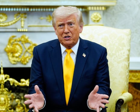 Donald Trump wearing a yellow tie, gesturing with his hands out as he takes questions from reporters in the Oval Office