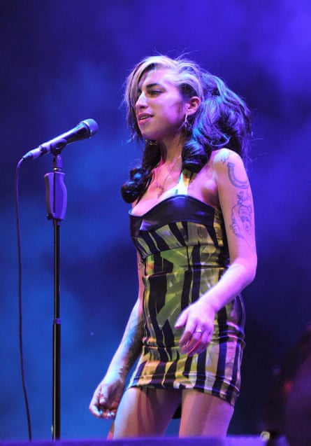A dishevelled woman with wild hair wearing a lime and black sleeveless mini dress singing