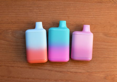 Multi-colored e-cigarettes - blue, pink, white and orange - on a wooden background