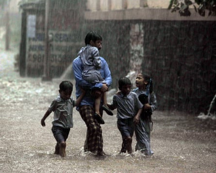 A man, soaked to the skin, carries one child and leads three more through a flooded street as the rain continues to pour