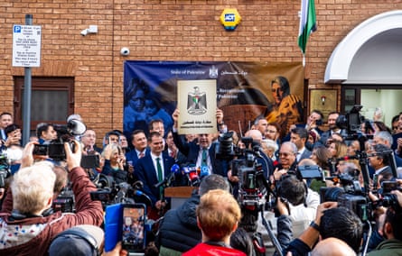 Zomlot lifts plaque with Palestinian eagle crest with press and people around