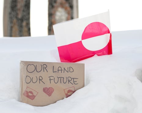 Signs reading “Our Land Our Future” in both English and Greenlandic rest in the snow alongside flags of Greenland.