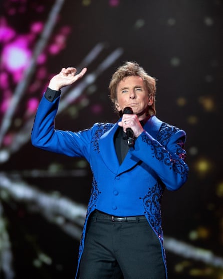 Manilow on stage in royal blue jacket with one hand in the air