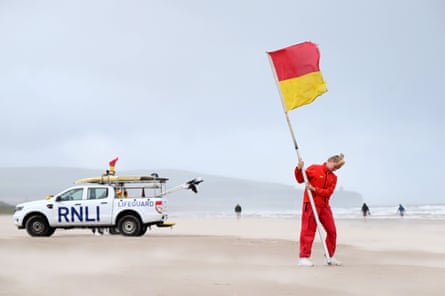 An RNLI vehicle on a beach while a lifeguard plants a warning sign in the sand in high winds. An RNLI vehicle on a beach while a lifeguard plants a warning sign in the sand in high winds.