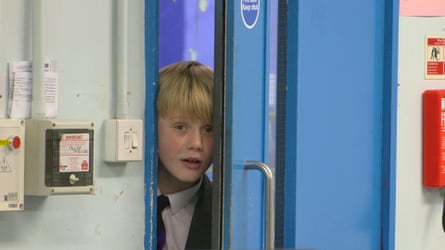 A blond boy pokes his head around a door.