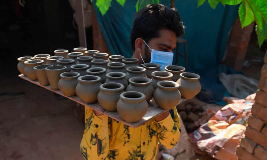 Potter Anilbhai Prajapati carries a tray of tea cups to be dried at a village workshop