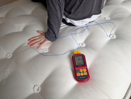 A man sits on a mattress next to an electric thermometer