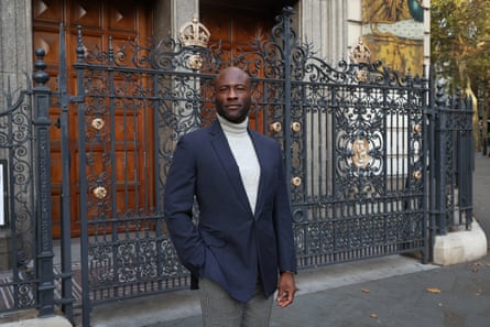 Bayo Randle stands in a navy blazer and turtleneck before an ornate wrought-iron gate