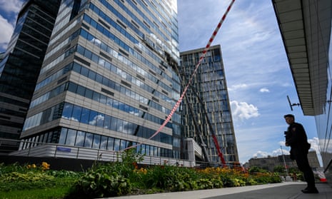 A police officer stands guard as crane workers dismantle debris from a skyscraper damaged by a drone in Moscow on Sunday