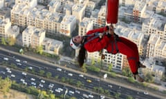 A woman dangles from a rope over buildings and a main road in Tehran