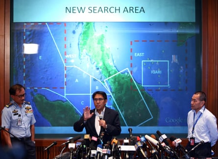 A Malay man speaks at a press conference in front of a large map as two other men, one in uniform, look on