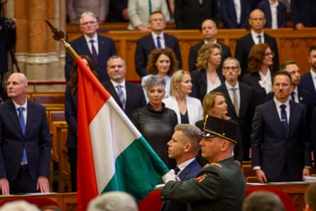Péter Magyar walks next to a serviceman carrying the Hungarian flag through the parliamentary chamber