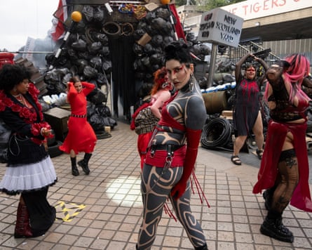 Female dancers with punk-style makeup, dyed hair and tattoos dance around a pile of tyres and a New Scotland Yard sign outside the Southbank Centre