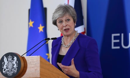 Prime minister gesticulates in front of a microphone, with European flag behind her