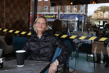 Clifford sits at cafe table with a disposable coffee cup on it, with street behind.