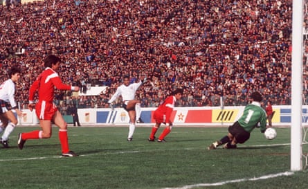 A black football player shoots past a goalkeeper as two defenders (and a young Gary Lineker) look on
