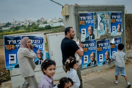 A Palestinian family walks past election campaign posters