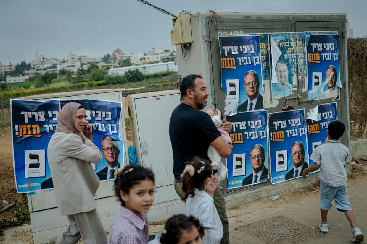 A Palestinian family walks past election campaign posters