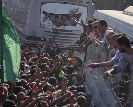Prisoners lean out of the windows of the buses as crowds gather to wave at them