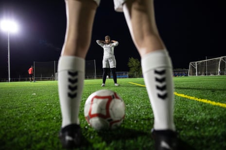 A football seen on the pitch between the feet on a female player with another female player in the distance