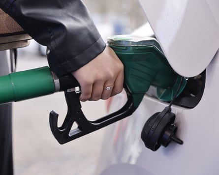 A closeup of a hand holding at petrol pump while filling up a white car