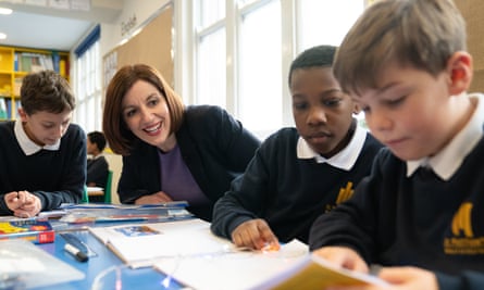 Bridget Phillipson with three primary schoolchildren at a desk in a classroom while they read
