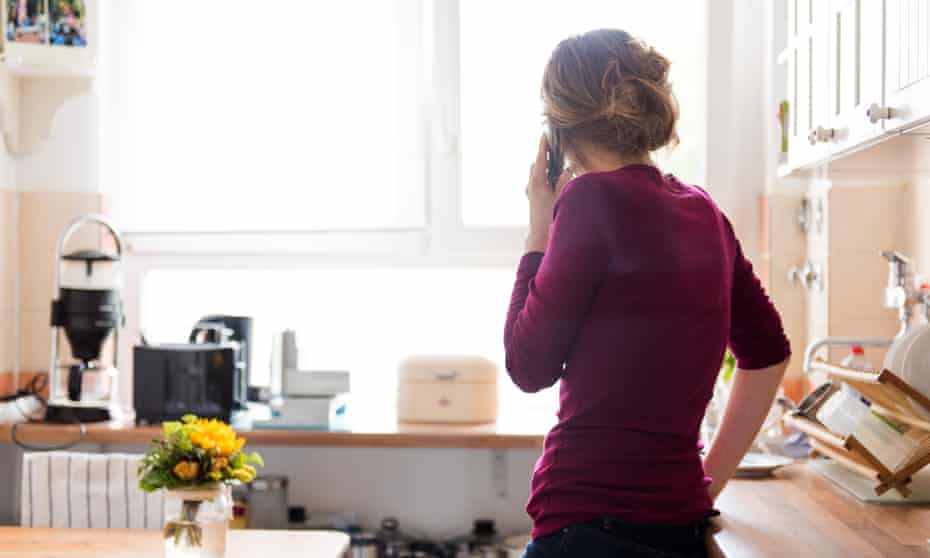 A young woman at home in the kitchen is using a telephone, while looking out of the window