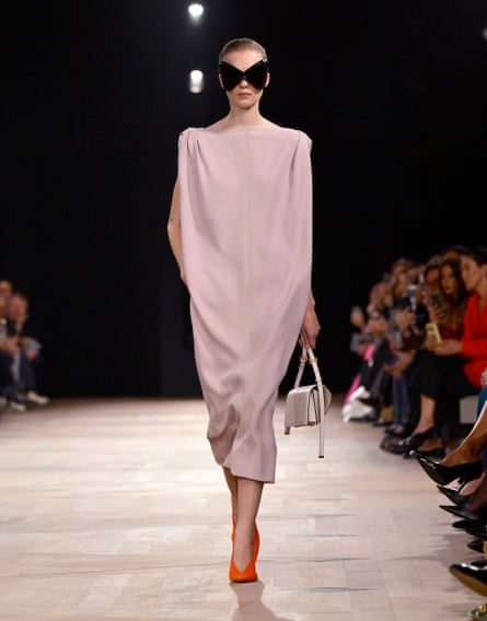 A woman wears a soft pink ankle-skimming sack dress and orange pumps – with apocalypse-chic wraparound bug-eye sunglasses