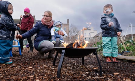 Women and children toast marshmallows around a firepit. 