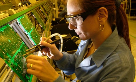 a woman worker wearing protective goggles solders a circuit board in a factory