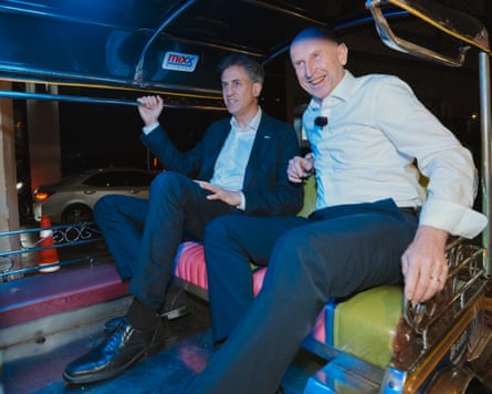 Ed Miliband and John Healey smile together inside a colourful tuk-tuk at night