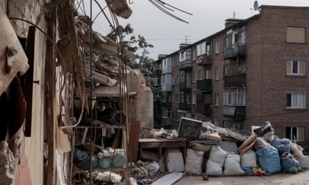 The side of a building completely ripped off, with shelving and a TV visible, and sand bags