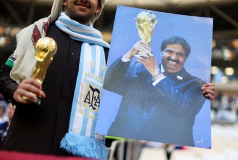 A fan in an Argentina holding a replica World Cup trophy and a photography of Qatar's Sheikh Hamad bin Khalifa. Sure, why not, eh?