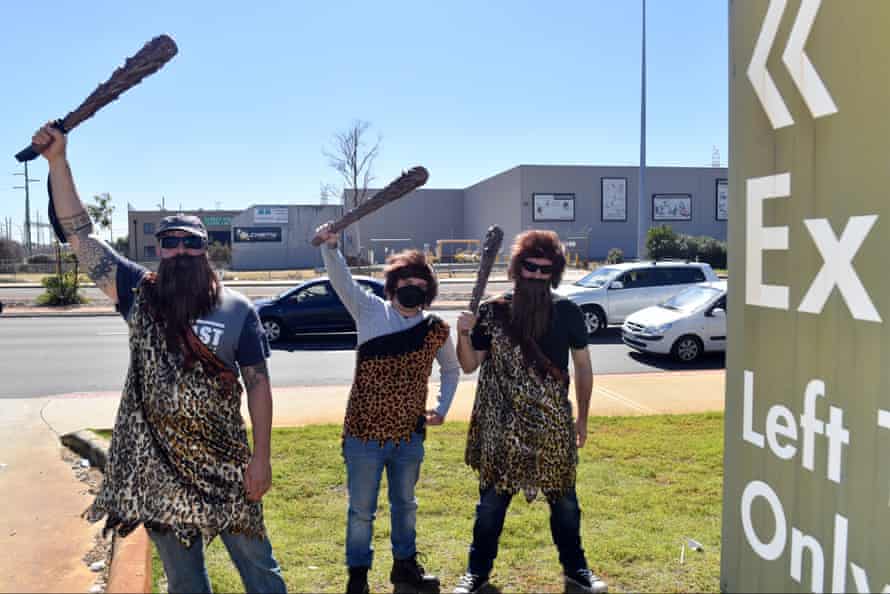 Three men dressed as cavemen wave plastic clubs as prime minister Scott Morrison visits Bunnings in Perth.